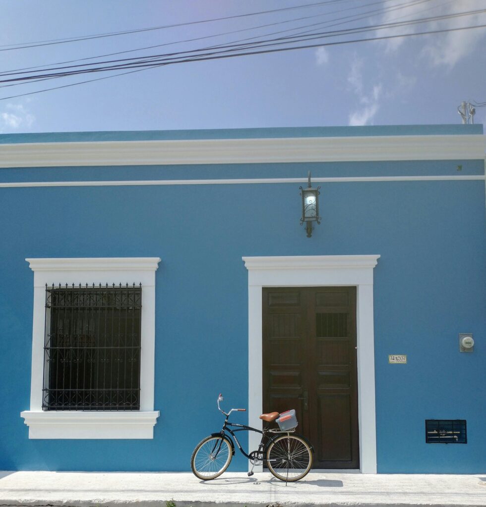 A vintage bicycle rests against a vibrant blue house wall in Mérida, Mexico showing Yucatán Real Estate Market.